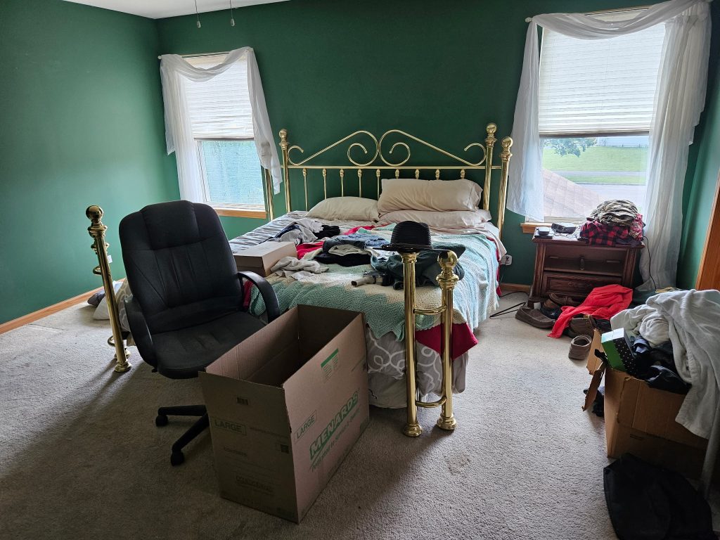 Bedroom with brass bed frame, office chair, dresser, and moving boxes before furniture removal by Junk Nurse in Aurora IL