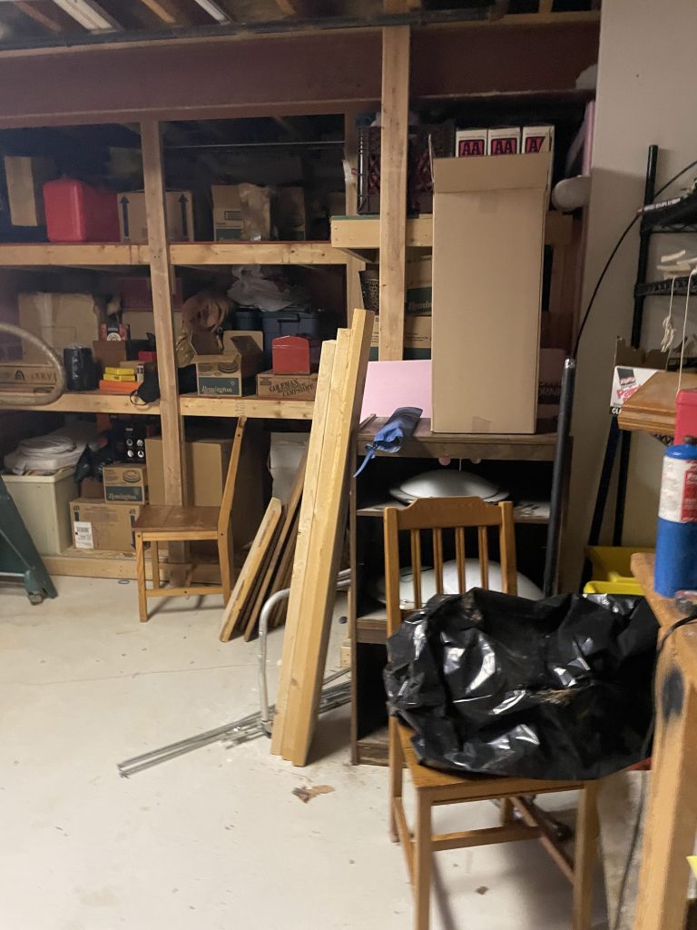 Cluttered basement with packed shelves and wooden boards before Junk Nurse cleanout in Aurora IL