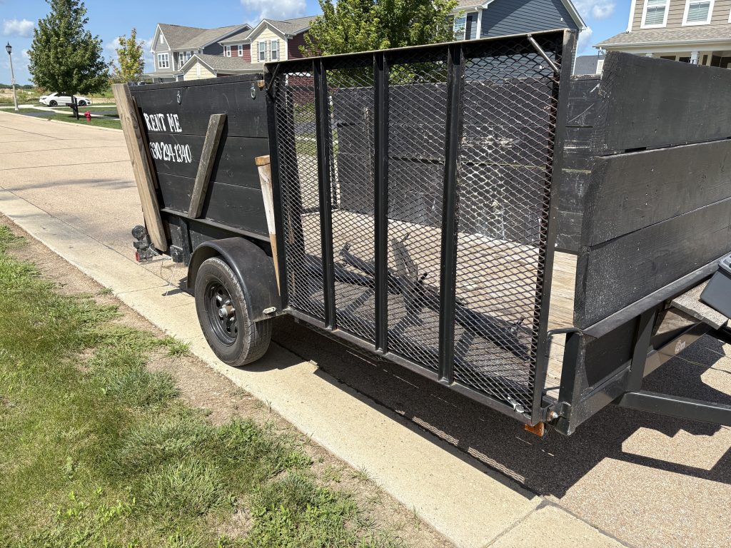 Junk Nurse branded open mesh trailer parked in a suburban neighborhood ready for a cleanout job near Warrenville IL