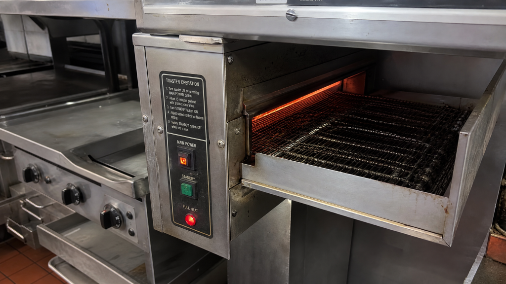 Commercial conveyor toaster with glowing heating elements in a restaurant kitchen cleared by Junk Nurse in Aurora IL
