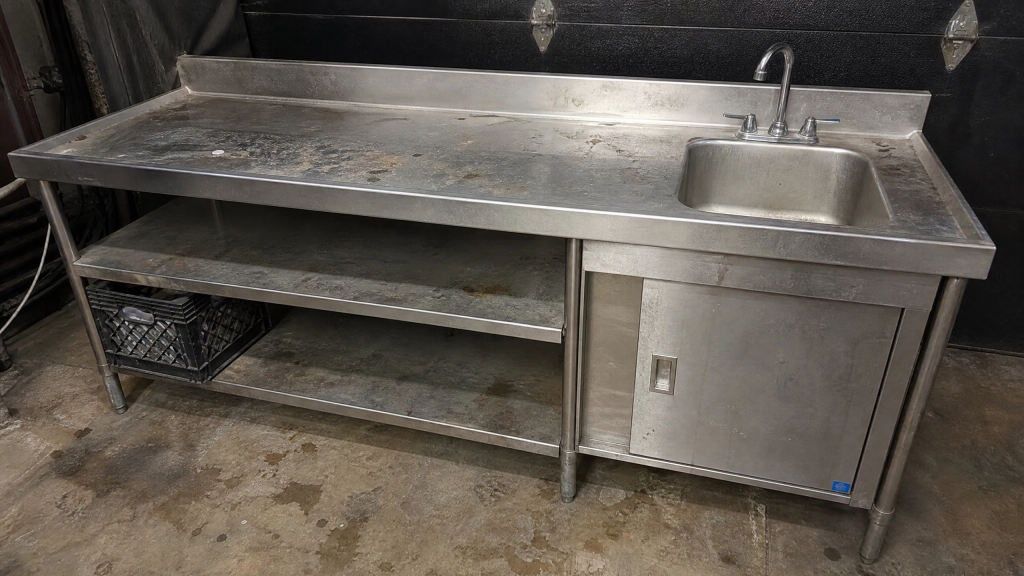 Stainless commercial prep table with integrated sink removed from a restaurant and staged for disposal by Junk Nurse in Aurora IL